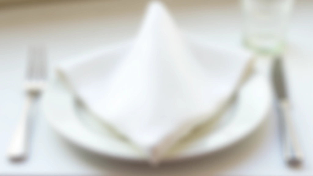 Elegant white napkin folded in simple triangle shape on formal dinner plate with silverware